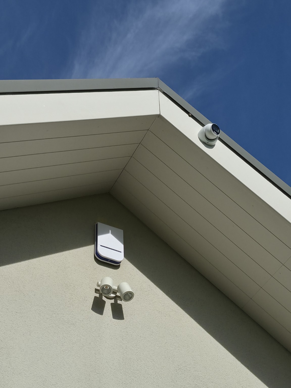 Security camera, alarm sensor, and floodlight installed on a house exterior